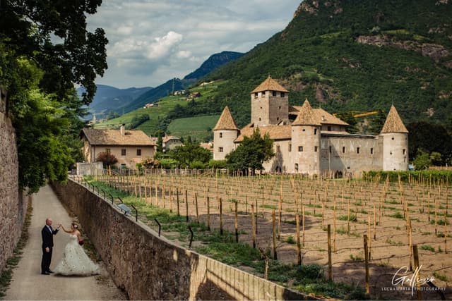 Coppia di sposi in cammino verso Castel Mareccio tra i vigneti