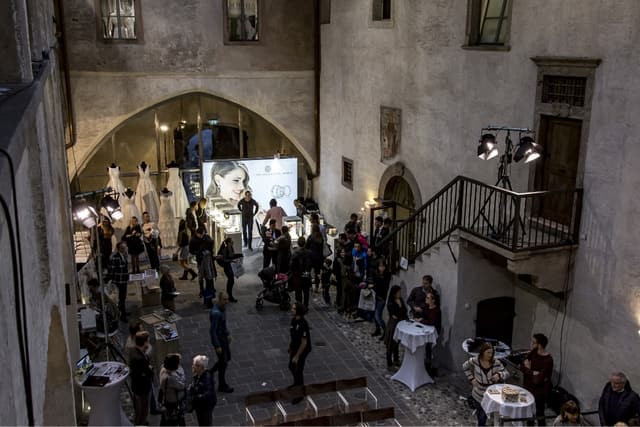 Visitatori nel cortile illuminato di Castel Mareccio tra abiti da sposa ed espositori